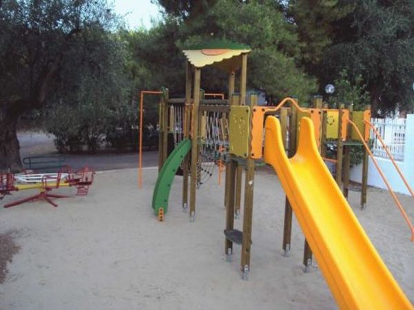 Parco giochi con scivolo arancione e altalene su sabbia.