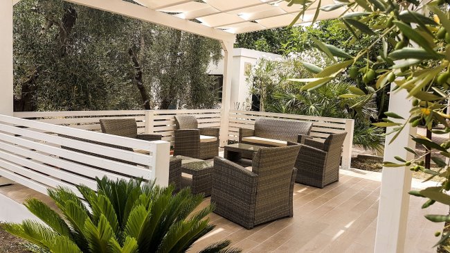 Terrazza con sedie in vimini e vegetazione intorno.