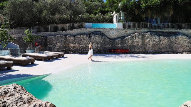 Piscina all'aperto con lettini e acqua turchese.
