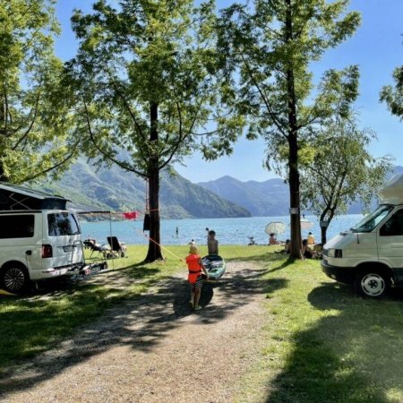 Parchi camper vicino al lago, persone e alberi.