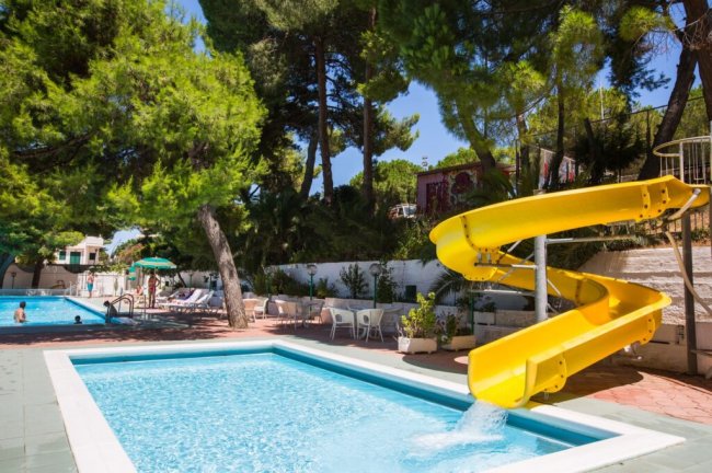 Piscina con scivolo giallo e alberi verdi.