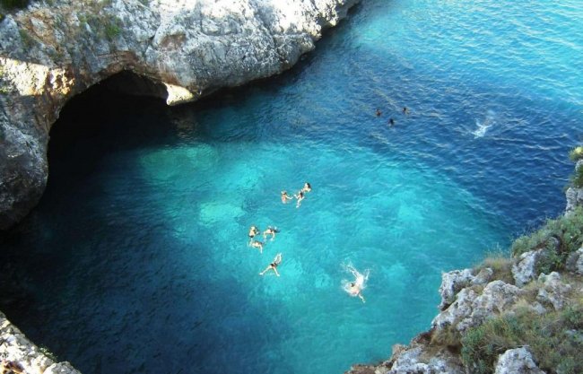 Persone nuotano in mare turchese vicino a una grotta.