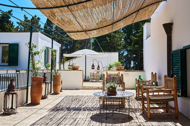 Terrazza con sedie in legno, tavolo e copertura in paglia.