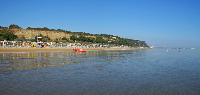 Spiaggia ampia e calma, vista mare con colline verdi sullo sfondo.