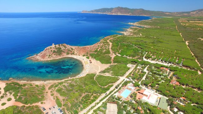 Vista dall'alto di una costa con spiaggia, vegetazione e mare blu.