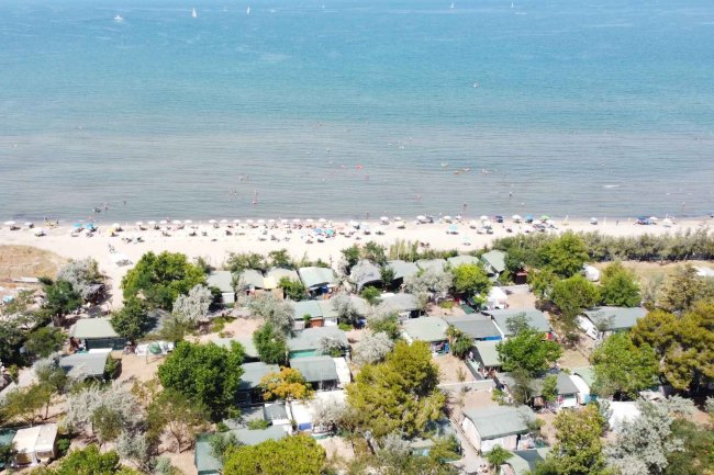 Spiaggia e mare con bungalow tra alberi.