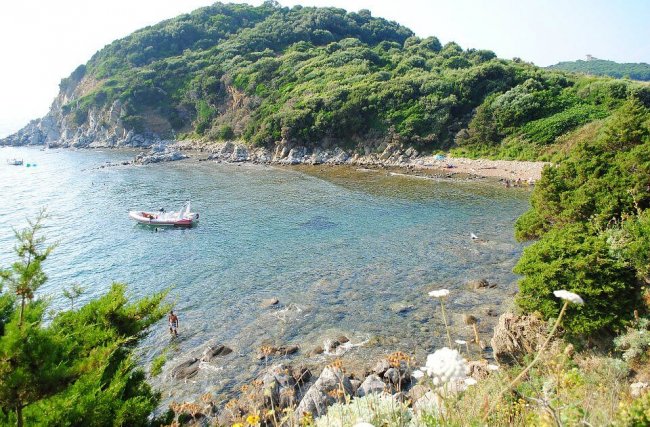 Baia rocciosa con vegetazione e una barca ancorata.