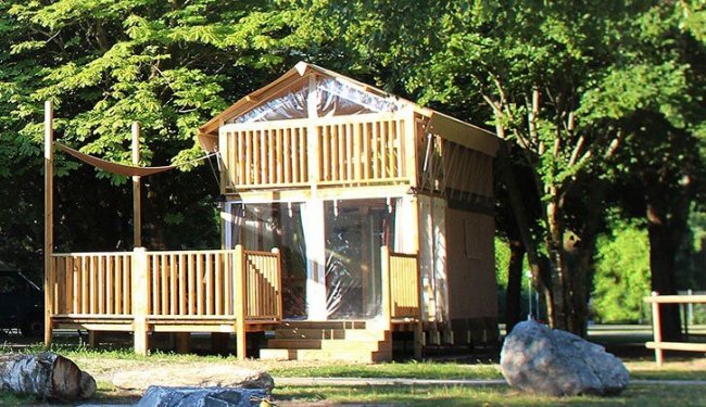 Casa di legno su due livelli con veranda, circondata da alberi.