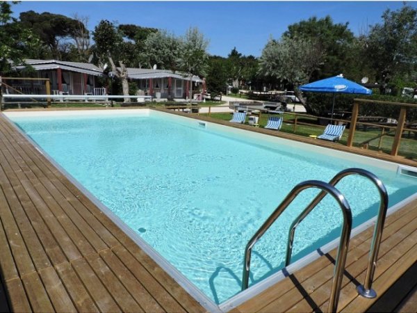 Piscina rettangolare con acqua blu, circondata da una piattaforma in legno e sdraio.