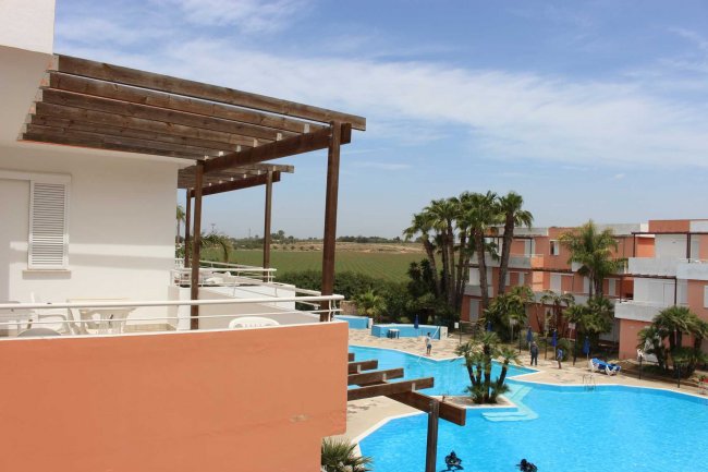 Piscina all'aperto con palme e edifici color pastello.