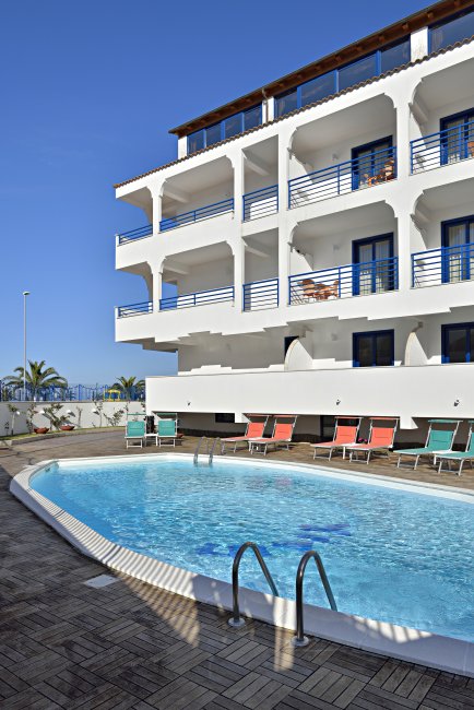 Piscina all'aperto con un edificio bianco a tre piani.