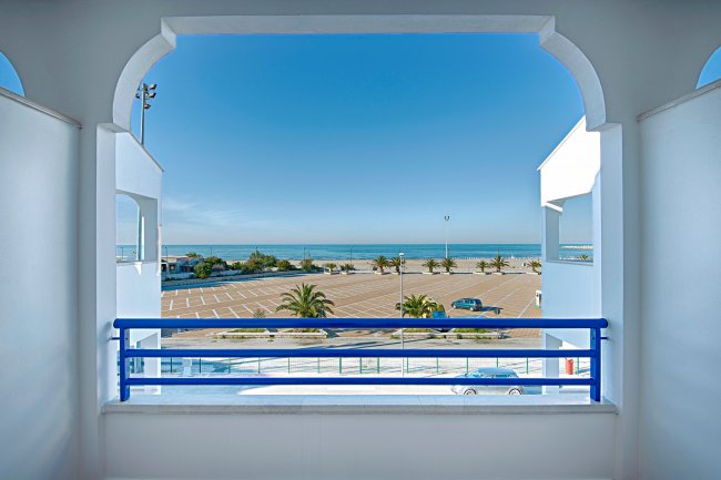 Vista su parcheggio, palme e mare.