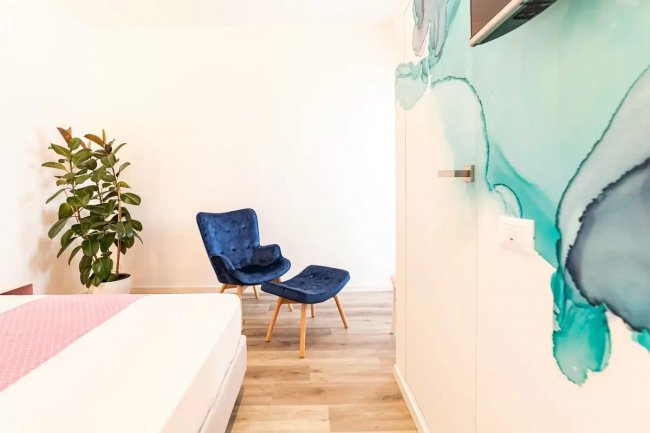 Stanza con sedia blu e pianta. Parete con arte astratta.