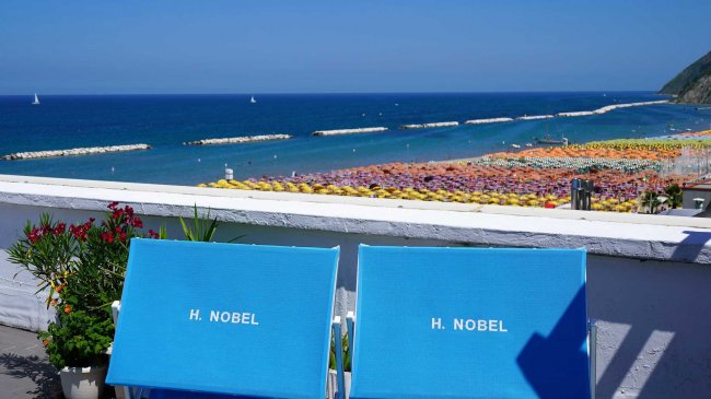 Due sedie blu su una terrazza con vista sul mare e ombrelloni colorati.
