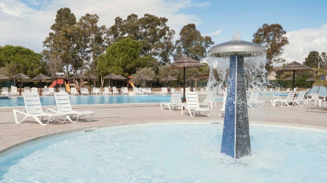 Fontana in piscina con lettini e ombrelloni.