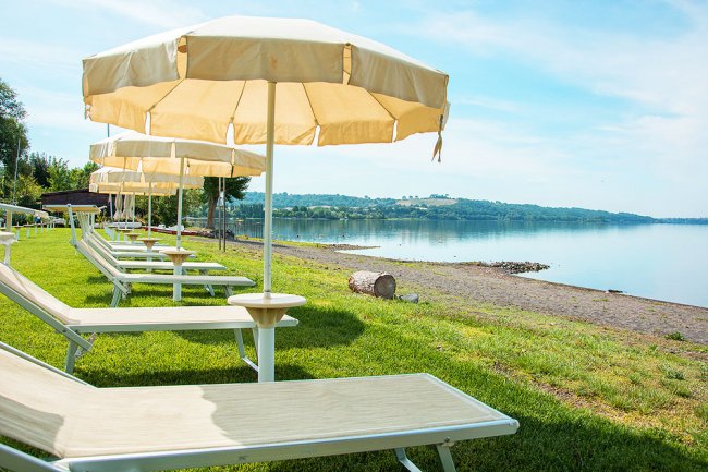 Lettini con ombrelloni su prato, vista lago.
