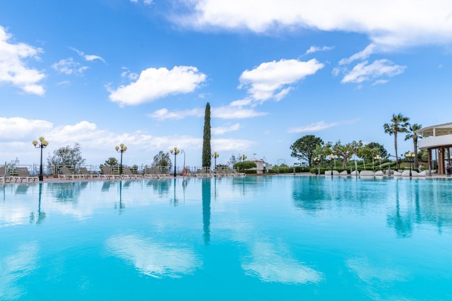 Piscina all'aperto con cielo azzurro e alberi intorno.