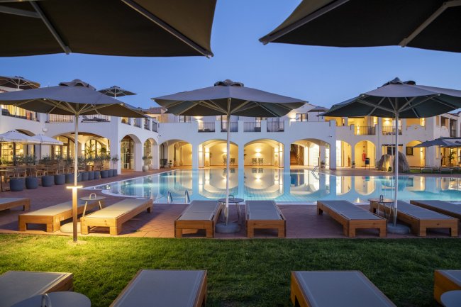 Piscina illuminata con lettini e ombrelloni al crepuscolo.