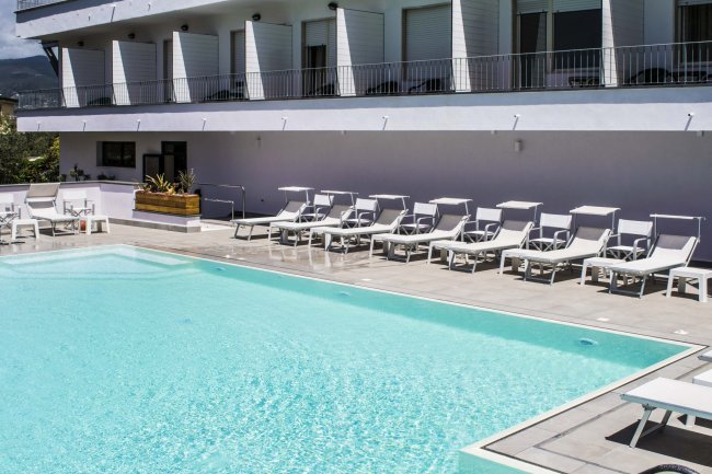 Piscina con sdraio bianche e hotel sullo sfondo.