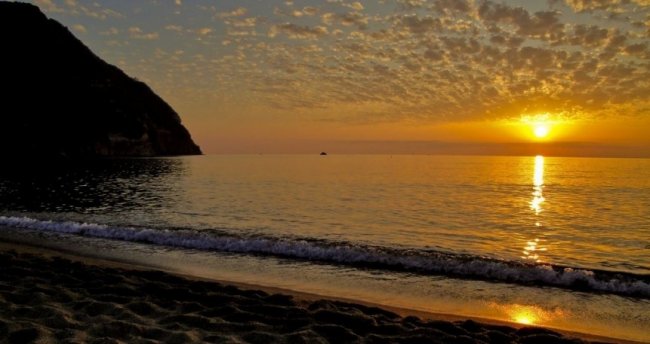 Tramonto su spiaggia e mare calmo.