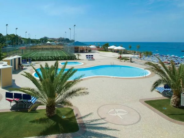 Piscina con palme, campo da calcio e vista mare.