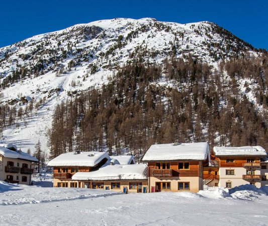 Case di legno innevate vicino a un pendio montano.