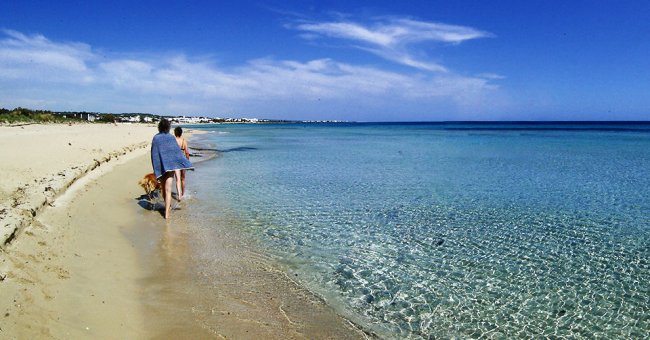 Persone camminano sulla spiaggia con mare cristallino.