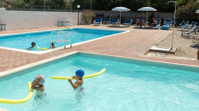 Due piscine con lettini e ombrelloni.