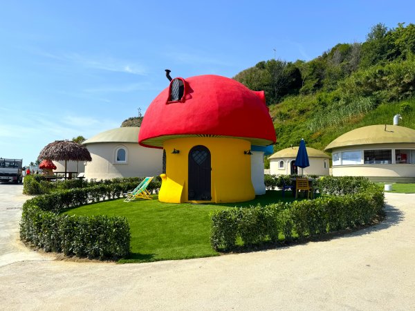 Casa a forma di fungo rosso con giardino e sedie a sdraio.