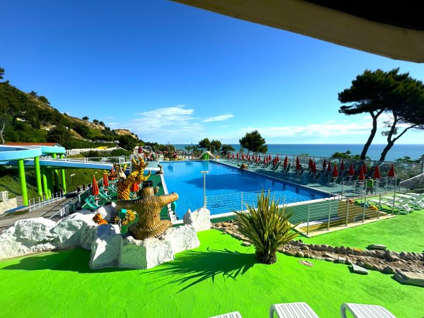 Piscina all'aperto con sdraio e ombrelloni rossi vicino al mare.