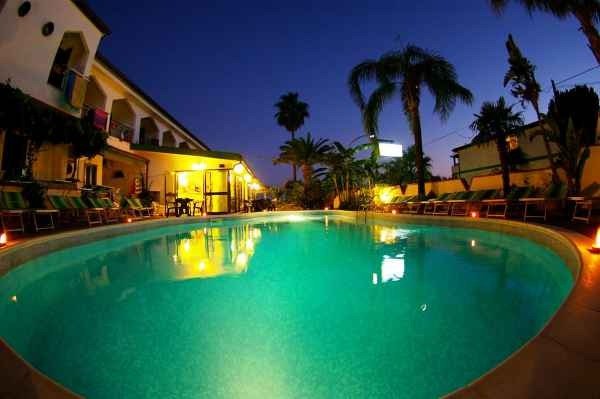 Piscina illuminata di sera con palme.