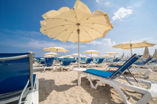 Spiaggia con lettini blu e ombrelloni beige.