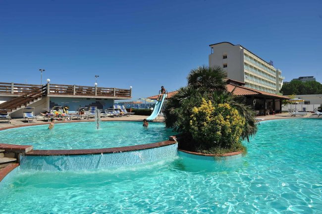 Piscina con scivolo e vegetazione centrale.