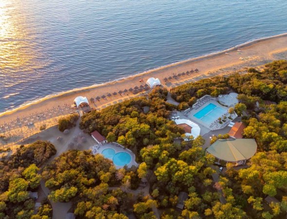 Spiaggia al tramonto con piscina tra alberi.