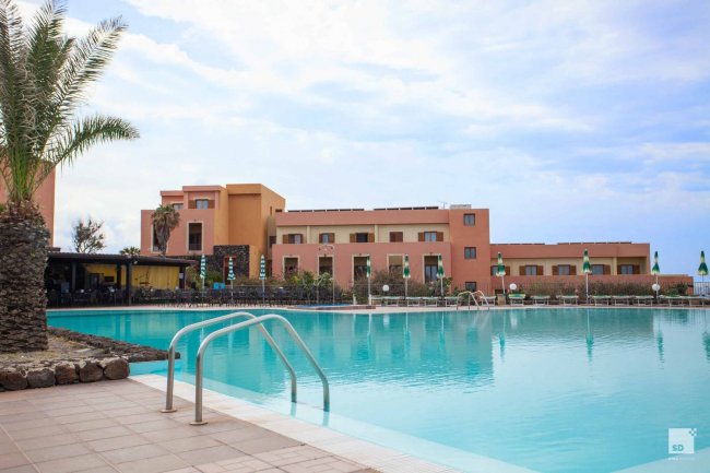 Piscina di fronte a un edificio con palme e cielo nuvoloso.