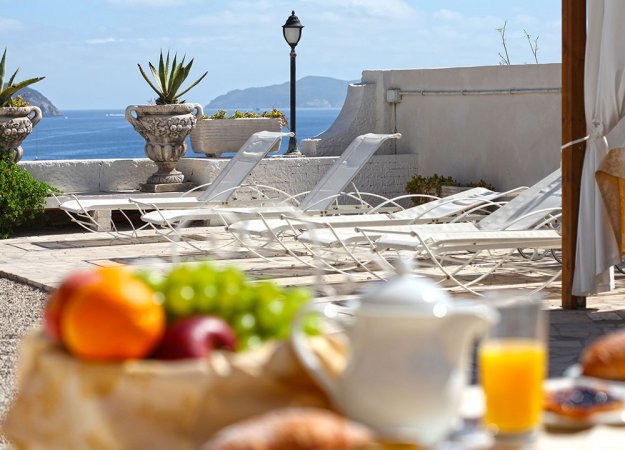 Terrazza vista mare, lettini bianchi e colazione.