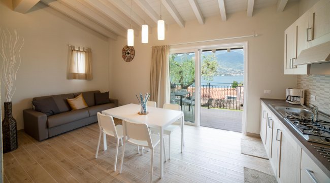 Soggiorno con tavolo e vista lago, cucina a destra.