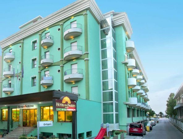 Un hotel verde con balconi bianchi e ingressi illuminati.
