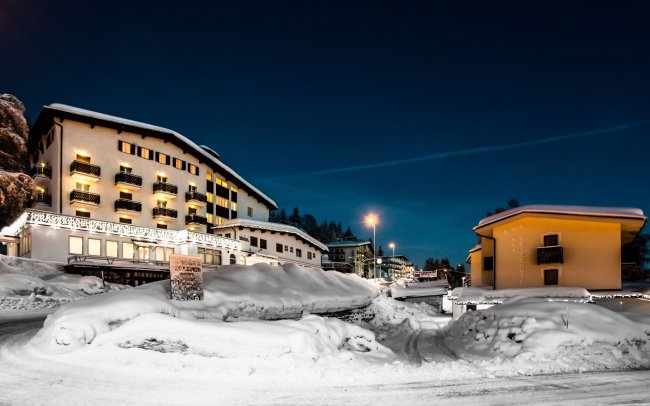 Hotel innevato di notte con luci accese.