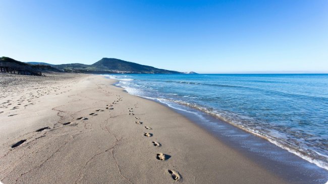 Orme su spiaggia con mare calmo e monte.