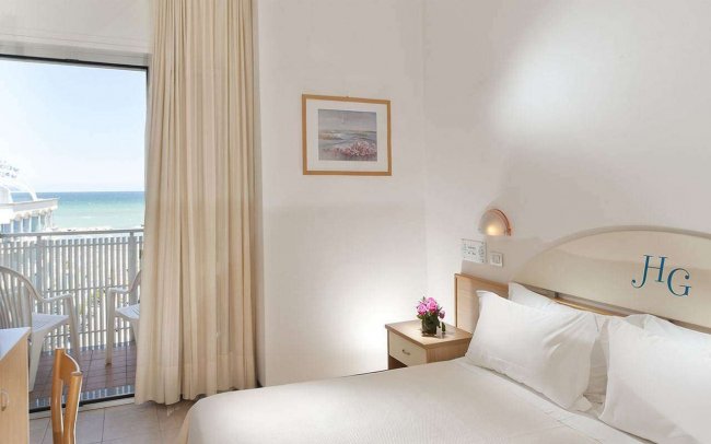 Camera d'hotel luminosa con vista sul mare dal balcone.