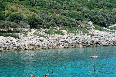 Costa rocciosa con acqua cristallina e persone che nuotano.