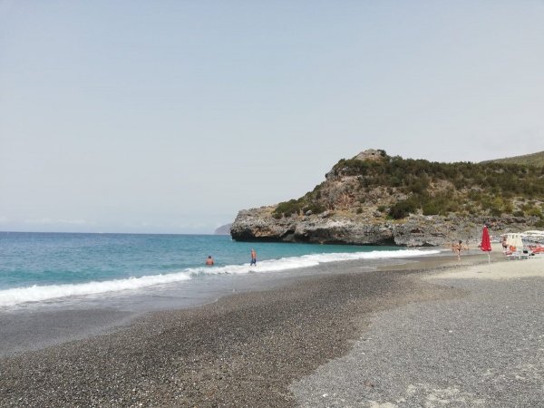 Spiaggia deserta con mare blu e scogliere.