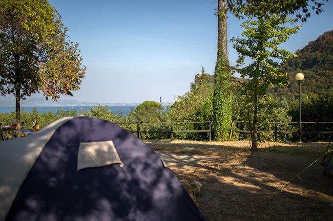 Tenda blu e vista sul mare, circondata da alberi.