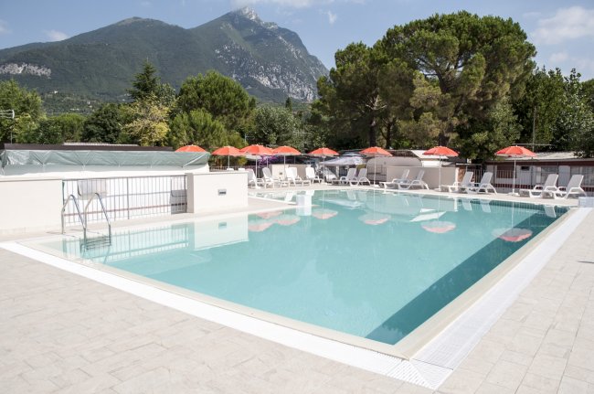 Piscina con ombrelloni rossi e montagne sullo sfondo.