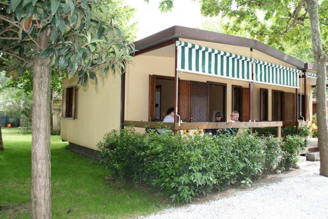 Bungalow con veranda e tende a righe, immerso nel verde.