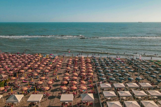 Ombrelloni beige e verdi su spiaggia vista mare.
