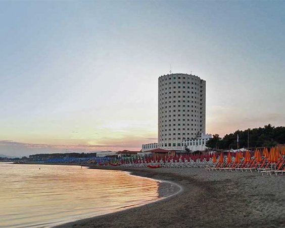Spiaggia al tramonto con grattacielo e ombrelloni.