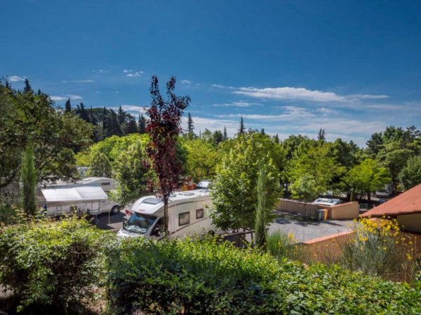 Camper in un campeggio verde con alberi e cielo blu.