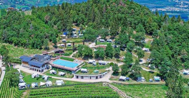 Camping con piscina circondato da alberi e camper.